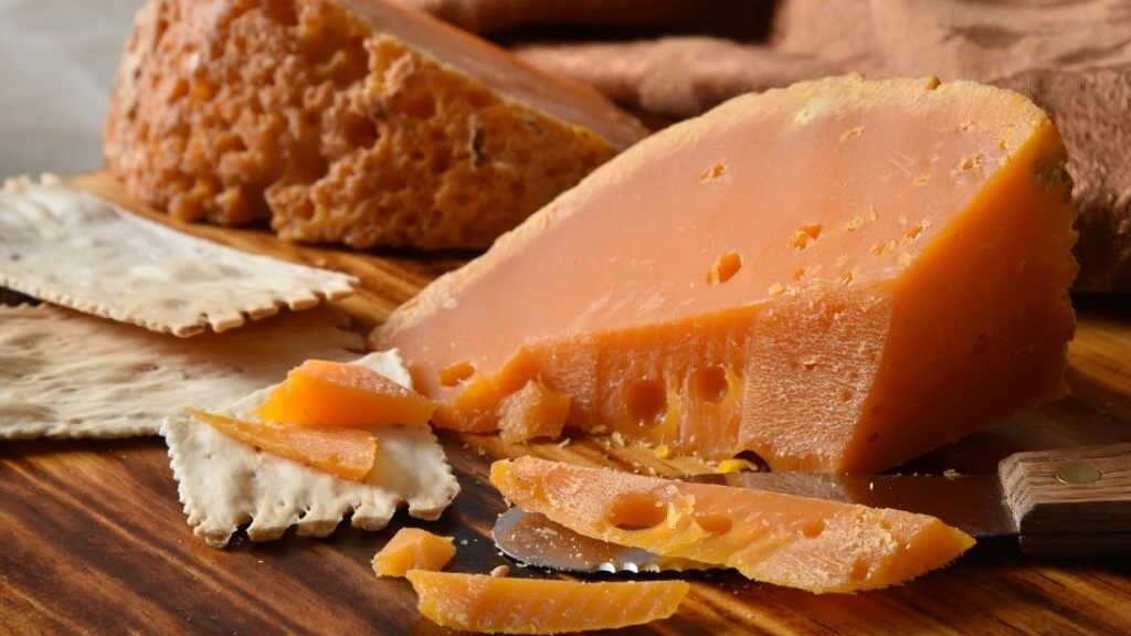 Un morceau de fromage Mimolette, présentant sa teinte orange distincte et sa texture unique.